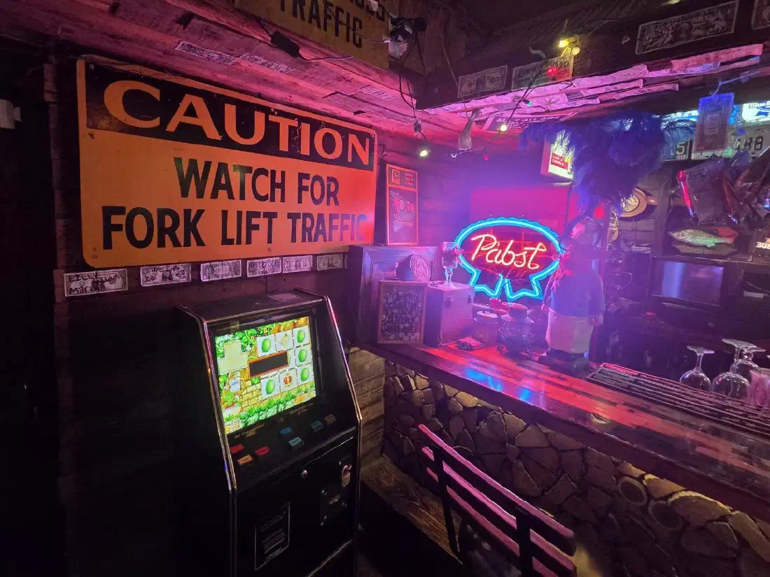 Inside the bar: a vintage caution sign, a Pabst neon glowing over the bar and dollar bills pinned to the walls