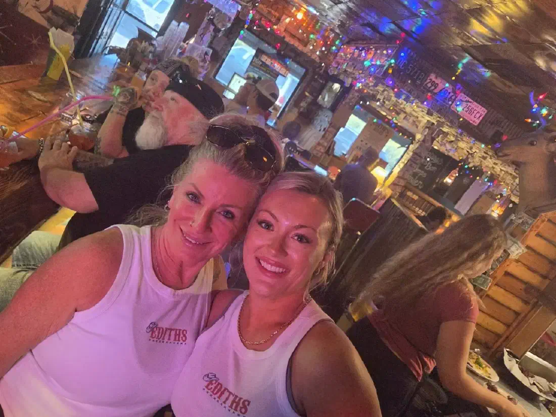 Two smiling Edith's servers in logo tank tops behind the bar