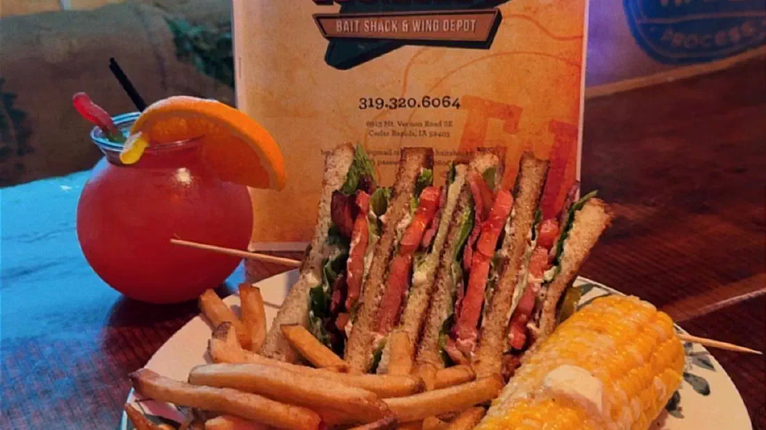 A club sandwich with fries, corn on the cob and a fruity cocktail in front of the Edith Lucielle's menu