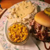 Pulled pork sandwich with grilled onions and BBQ sauce, mashed potatoes and corn