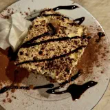 Square of house tiramisu dusted with cocoa, drizzled with chocolate, with whipped cream